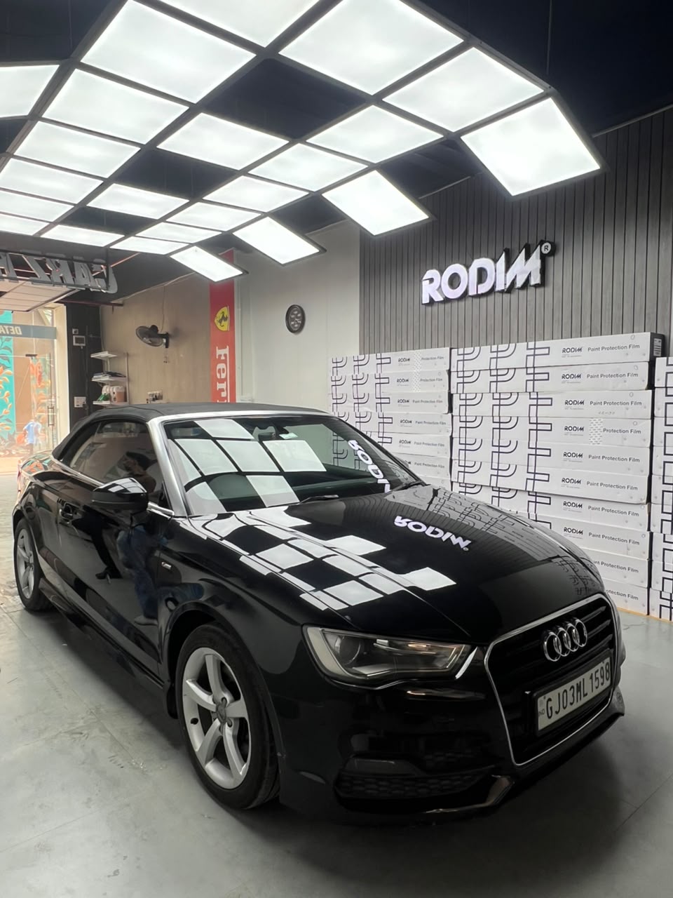 Black Audi convertible inside the Carz Hub studio beside stacked Rodim paint protection film boxes